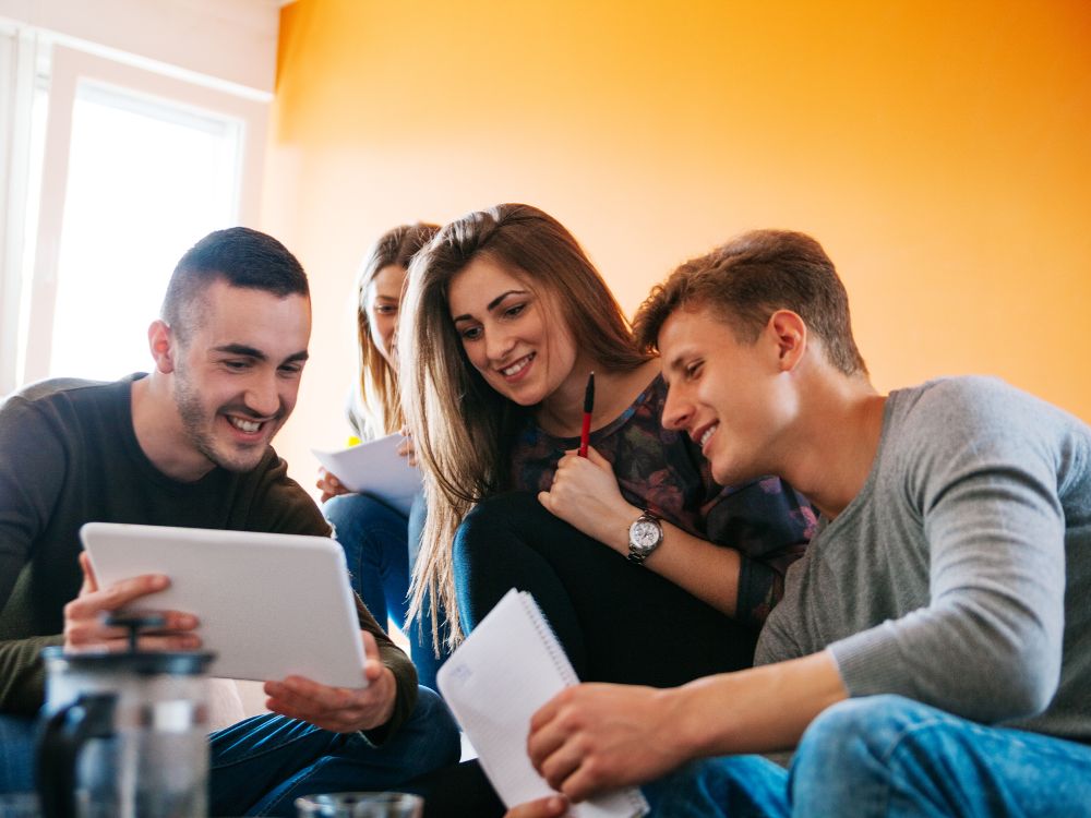 Grupo de estudantes reunidos ao redor de um tablet, simbolizando colaboração e estratégias de ações comerciais para captação de alunos.