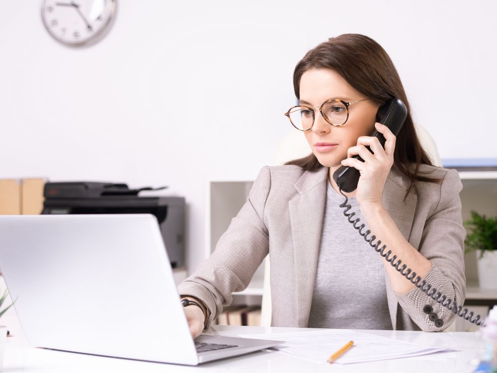 Mulher ao telefone diante de notebook. Atendimento integrado ao sistema de controle de matrículas em instituições educacionais.