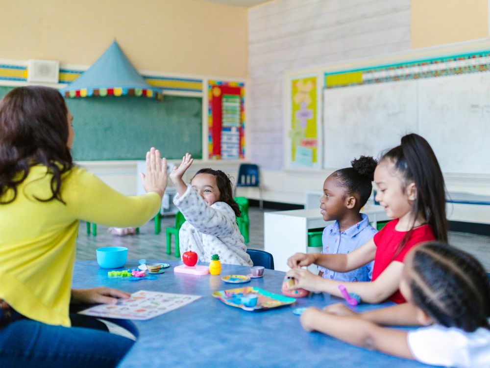 Professora interagindo com crianças em atividade lúdica, representando gestão da aprendizagem em sala de aula.