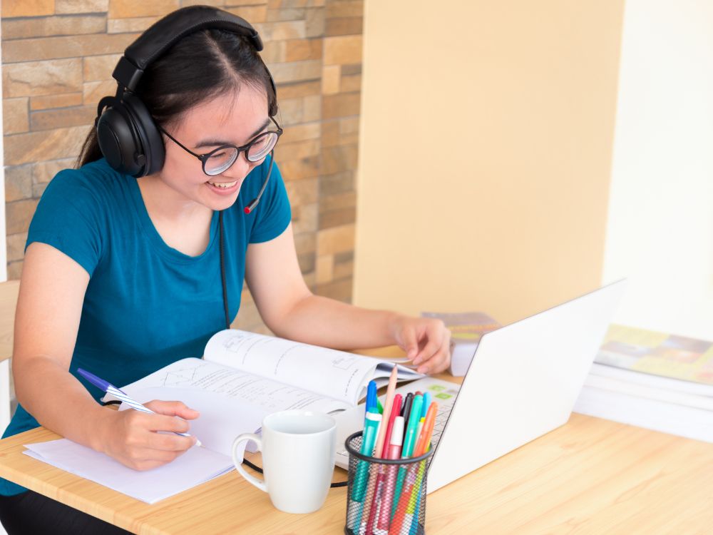 Estudante em aula online com fones e caderno, representando o impacto do novo marco regulatório do EaD nas atividades síncronas obrigatórias.