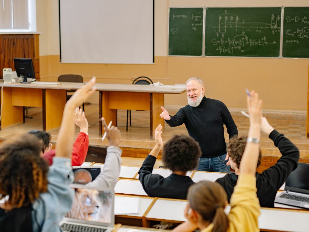 Docente conduzindo aula participativa com alunos levantando as mãos reflete na prática o que é gestão de sala de aula eficiente e bem estruturada.