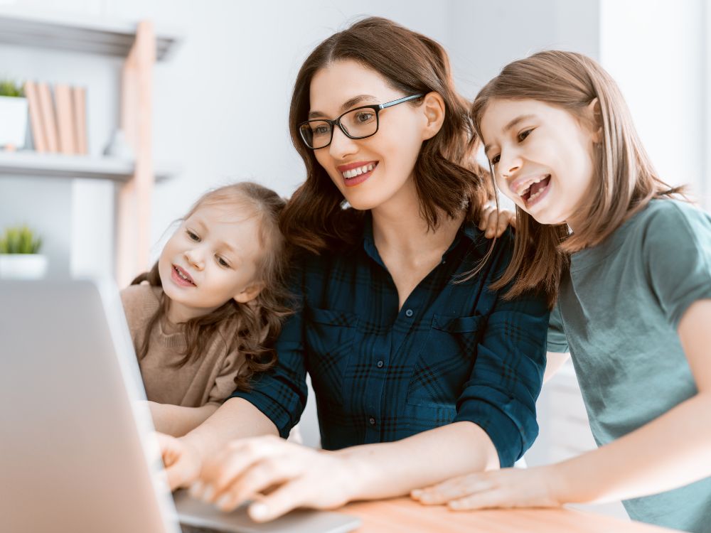 Mãe e duas filhas acessam informações escolares pelo notebook com auxílio de plataforma de gestão escolar integrada ao aplicativo da instituição.