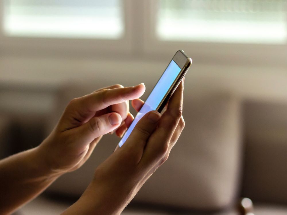 Pessoa utilizando aplicativo educacional no celular em ambiente residencial, interagindo com a tela sensível ao toque