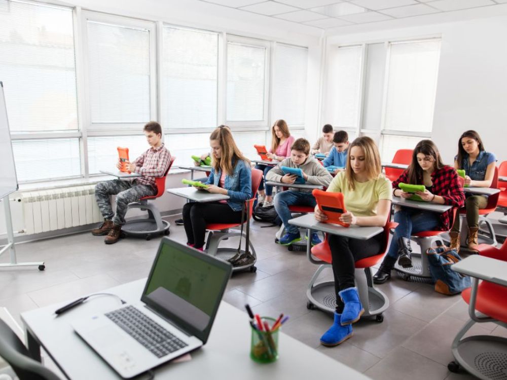 Turma de alunos usando tablets em sala moderna, representando o que é educação digital e a integração de tecnologia no ensino para maior engajamento.