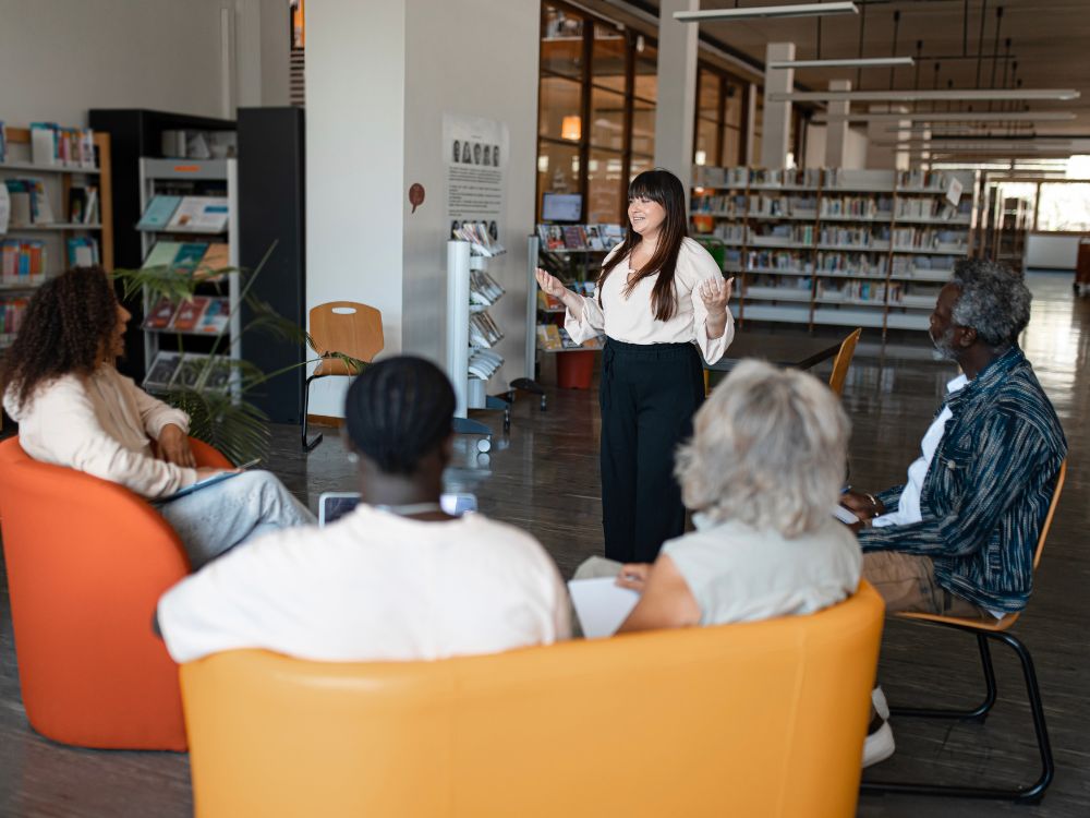 Grupo de adultos em uma biblioteca participando de uma reunião ou formação sobre estratégias para organizar escola.