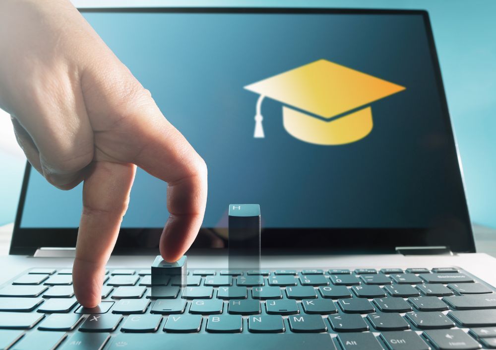 Conceito de software para faculdade mostrado em um laptop com ícone de formatura na tela e dedos simulando uma caminhada sobre o teclado, representando o acesso digital à educação superior.