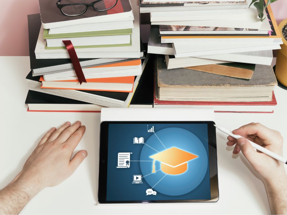 Tablet sobre a mesa com ícone acadêmico e pilhas de livros ao redor, simbolizando sistemas escolares para alunos que integram tecnologia e estudo.