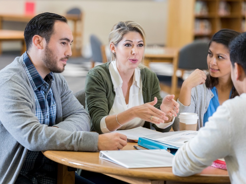 Grupo de pessoas reunidas em torno de uma mesa discutindo ideias e trocando opiniões durante uma reunião de trabalho sobre o resultado da analise de dados educacionais.