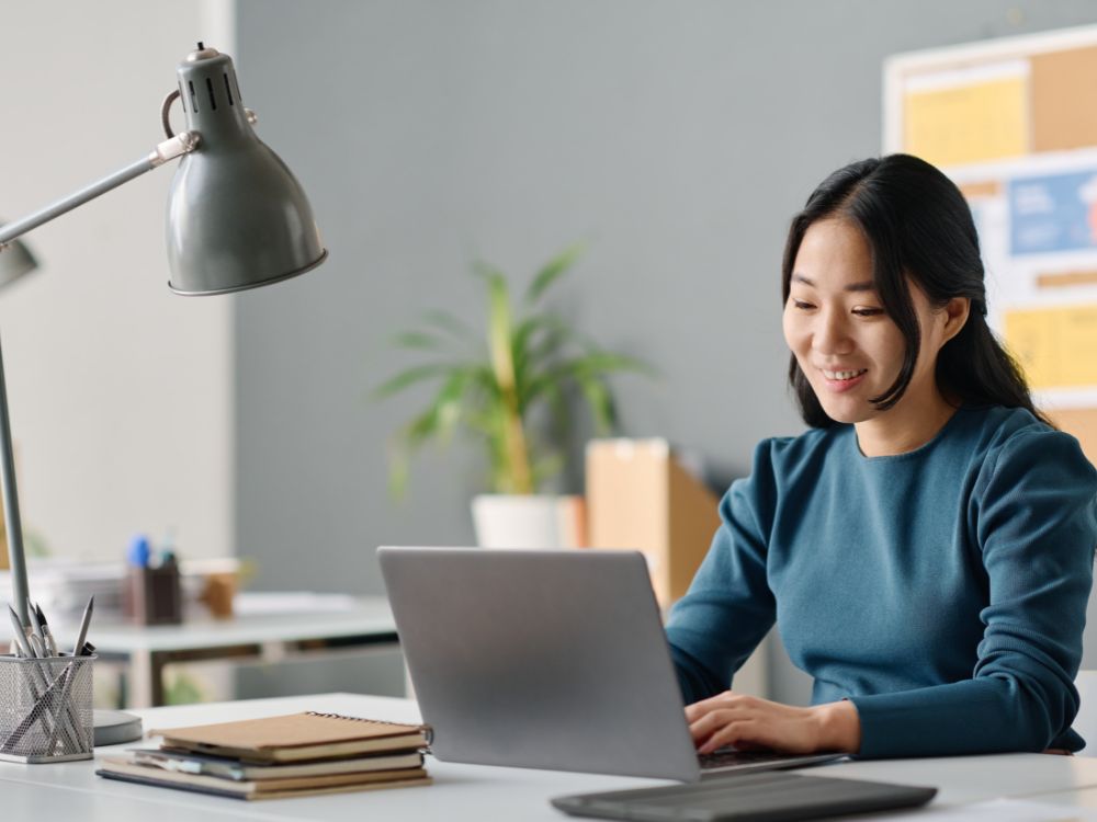 Profissional sorridente utilizando uma Plataforma de Gestão Educacional no computador para aprimorar a organização e o desempenho da instituição de ensino.