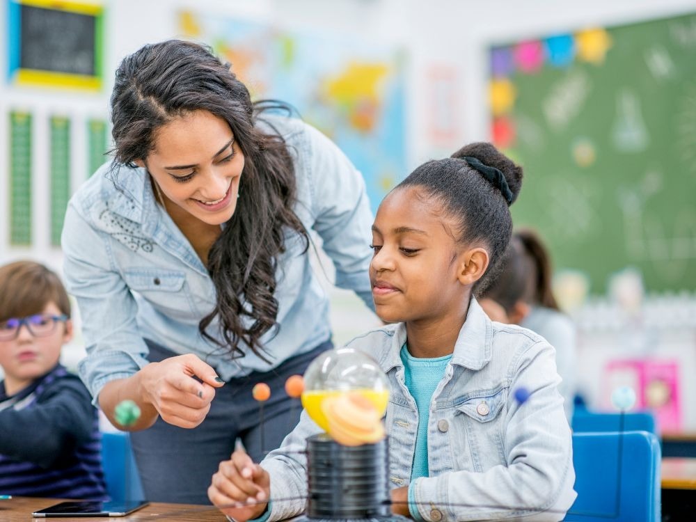 Educadora auxilia aluna em experiência prática, exemplo inspirador de como avaliar professores com foco em aprendizagem significativa.