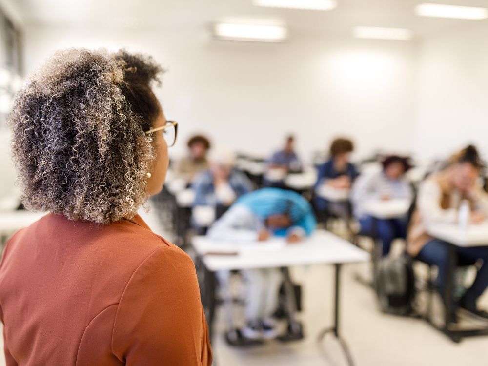 Professora observando alunos em sala de aula, representando a gestão eficiente com o uso de um Sistema para Controle de Notas e Faltas.