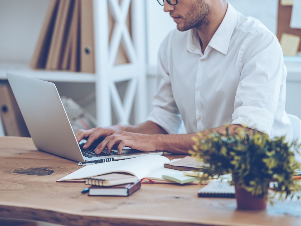 Homem usando notebook em um escritório organizado, representando a análise e o controle de processos administrativos na gestão escolar.