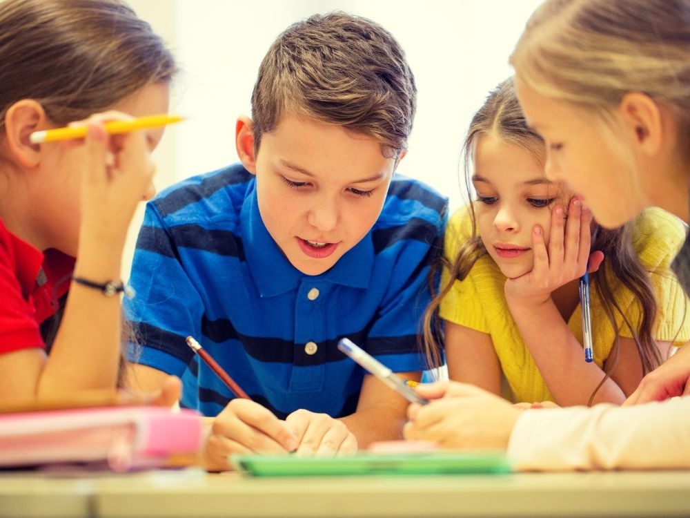Crianças estudando em grupo e desenvolvendo habilidades de leitura e escrita, fundamentais para os principais indicadores educacionais.