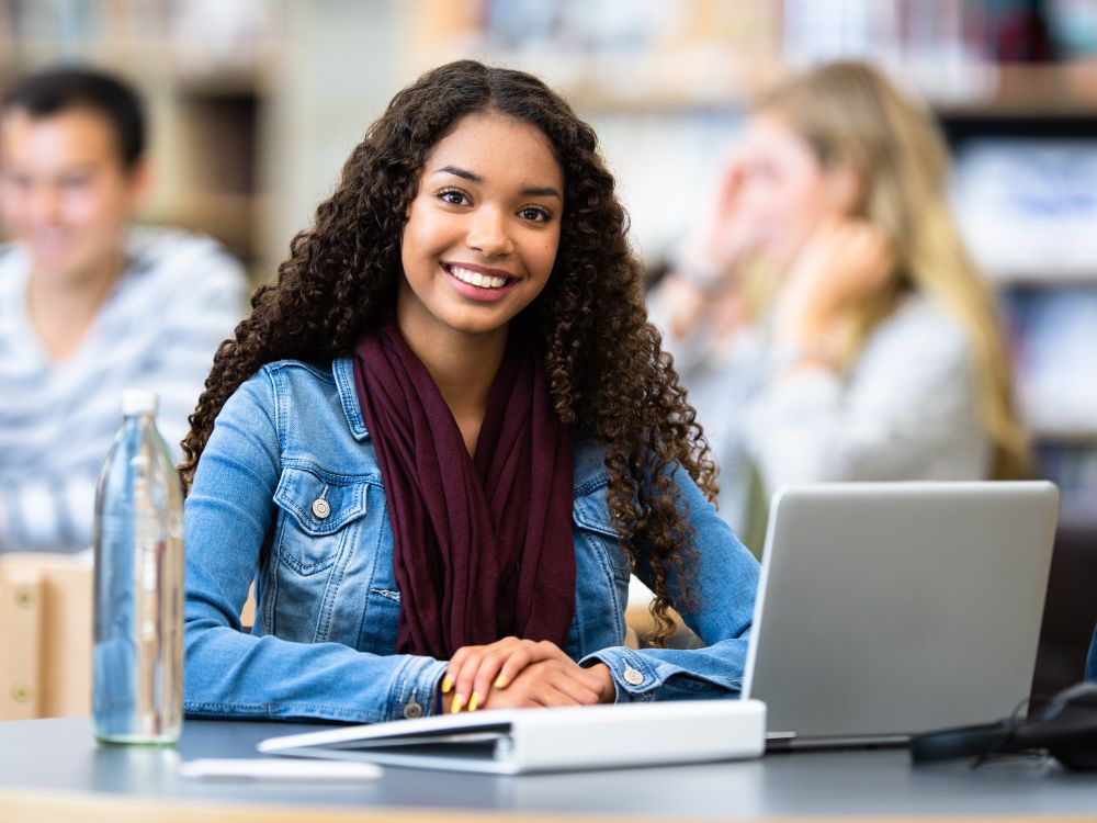 Estudante sorridente usando notebook em ambiente escolar, representando o uso do portal do aluno e responsável no dia a dia acadêmico.