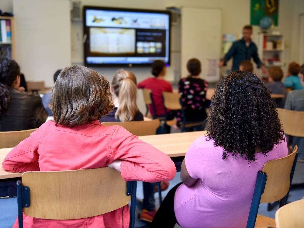 Alunos assistindo aula com professor e recursos digitais, reforçando a importância da experiência do aluno na educação moderna.