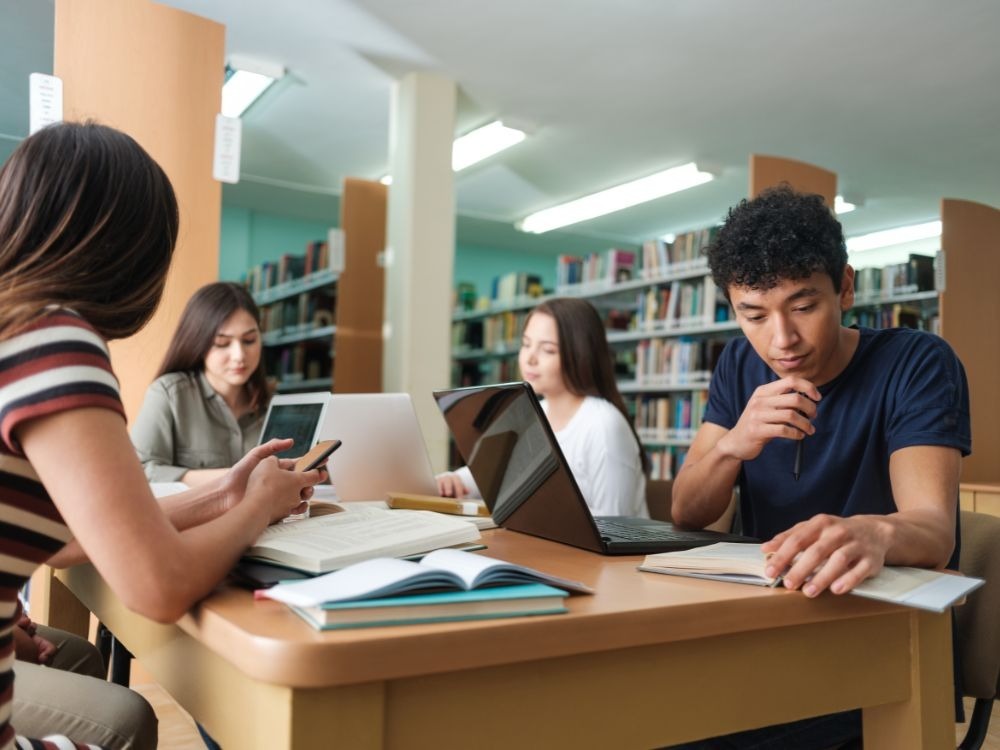Grupo de estudantes estudando juntos em biblioteca, representando práticas que garantem uma boa experiência do aluno na educação.