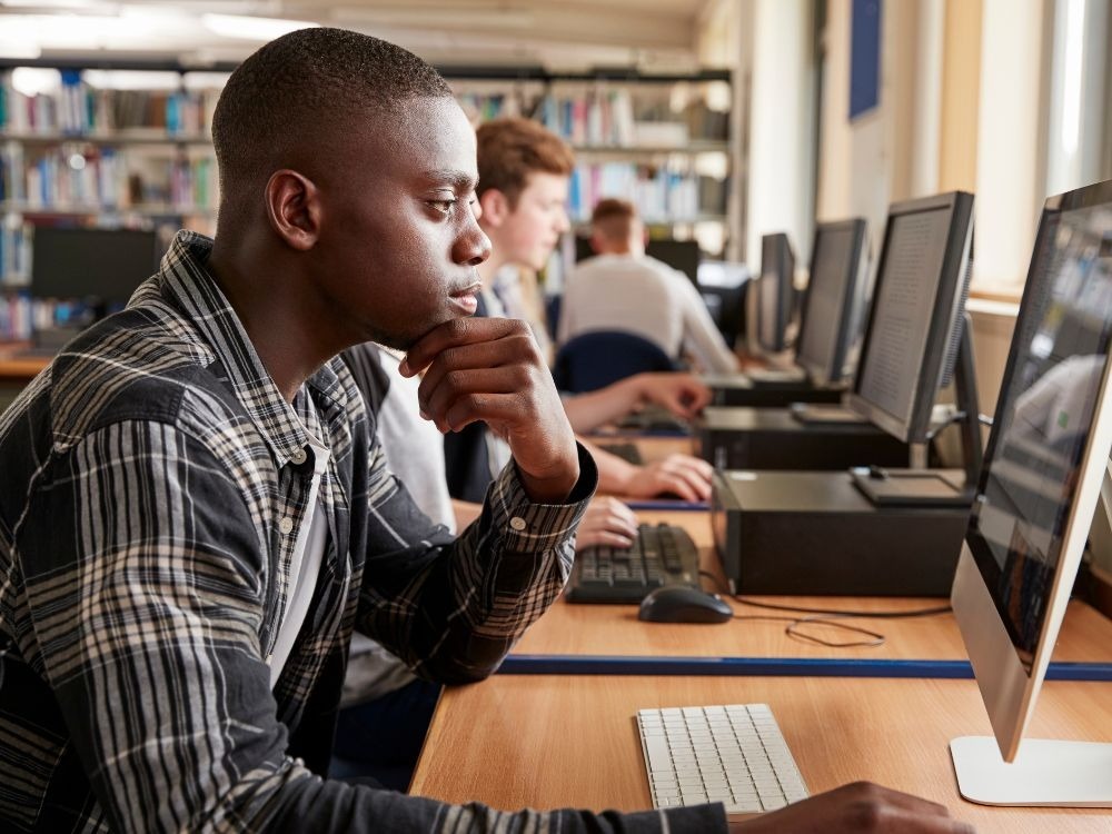 Estudantes utilizando computadores em laboratório escolar, representando a aplicação de ferramentas digitais na educação para aprendizagem tecnológica.