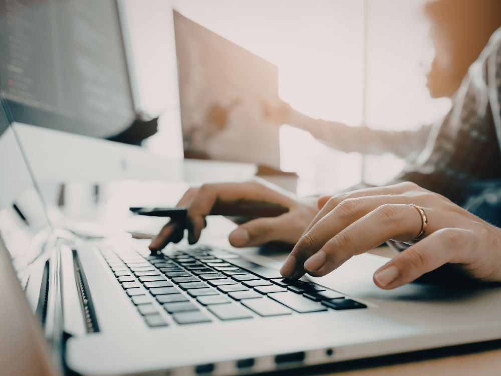 Pessoas digitando em computador durante análise de informações acadêmicas, ilustrando processos de Ajuste de Matrículas em ambiente digital.