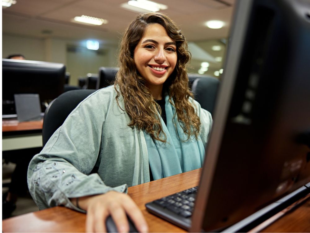 Profissional utilizando computador em ambiente educacional, representando a Automação de Processos Acadêmicos na rotina administrativa de instituições de ensino.