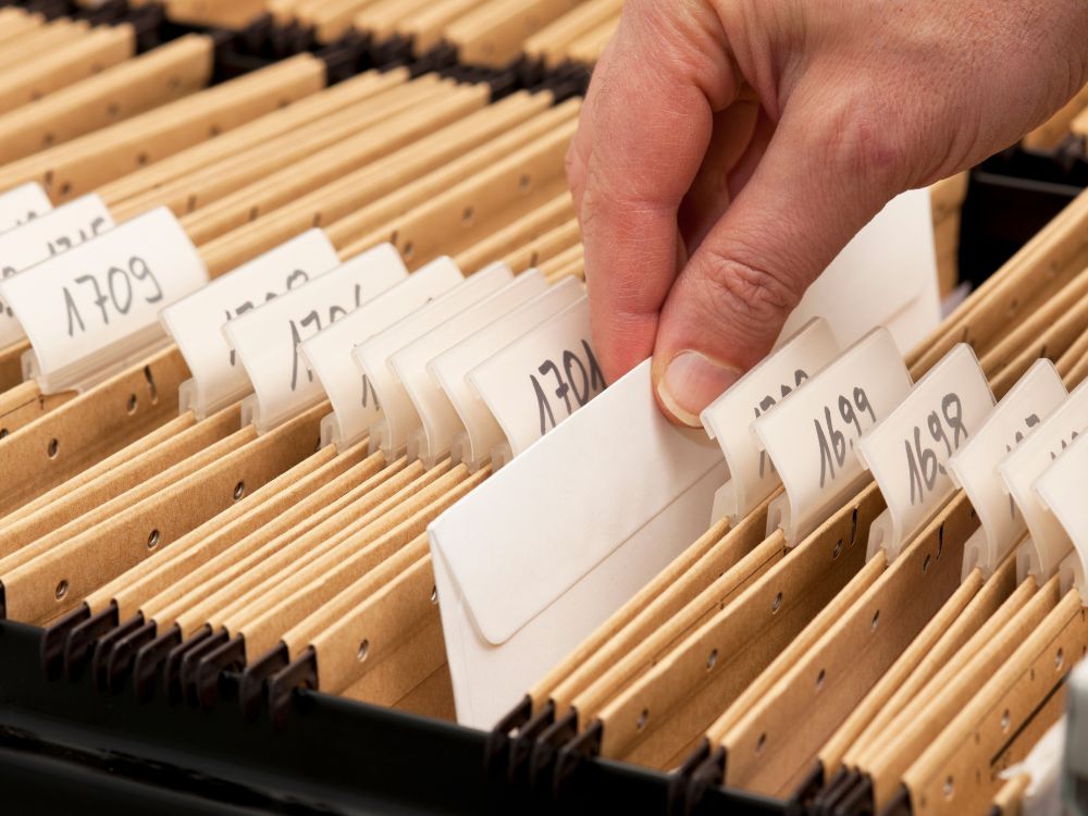 Mão organizando pastas físicas identificadas, representando etapas essenciais de Como organizar arquivo escolar com documentos impressos.