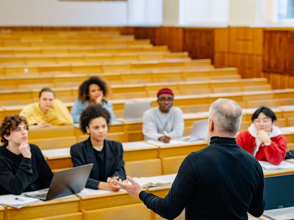 Sala de aula com professor e alunos universitários, cenário que representa debates sobre evasão no ensino superior.