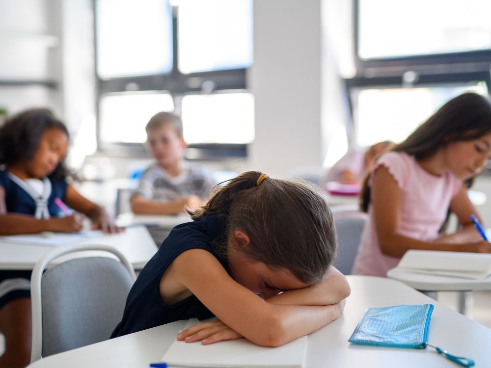 Aluna desmotivada com a cabeça na mesa durante aula, situação que evidencia comportamento ligado aos indicadores de evasão escolar.