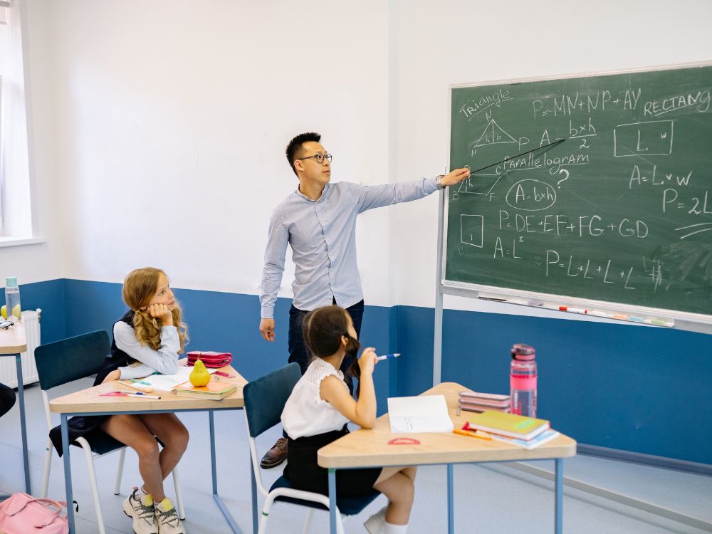 Professor explicando conteúdo no quadro para alunos atentos, etapa importante do planejamento escolar focada na execução das aulas.