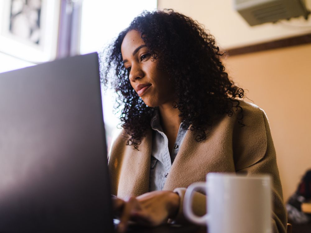 Mulher utilizando notebook em ambiente interno, representando a comunicação na escola por meio da tecnologia, plataformas digitais e ensino online.